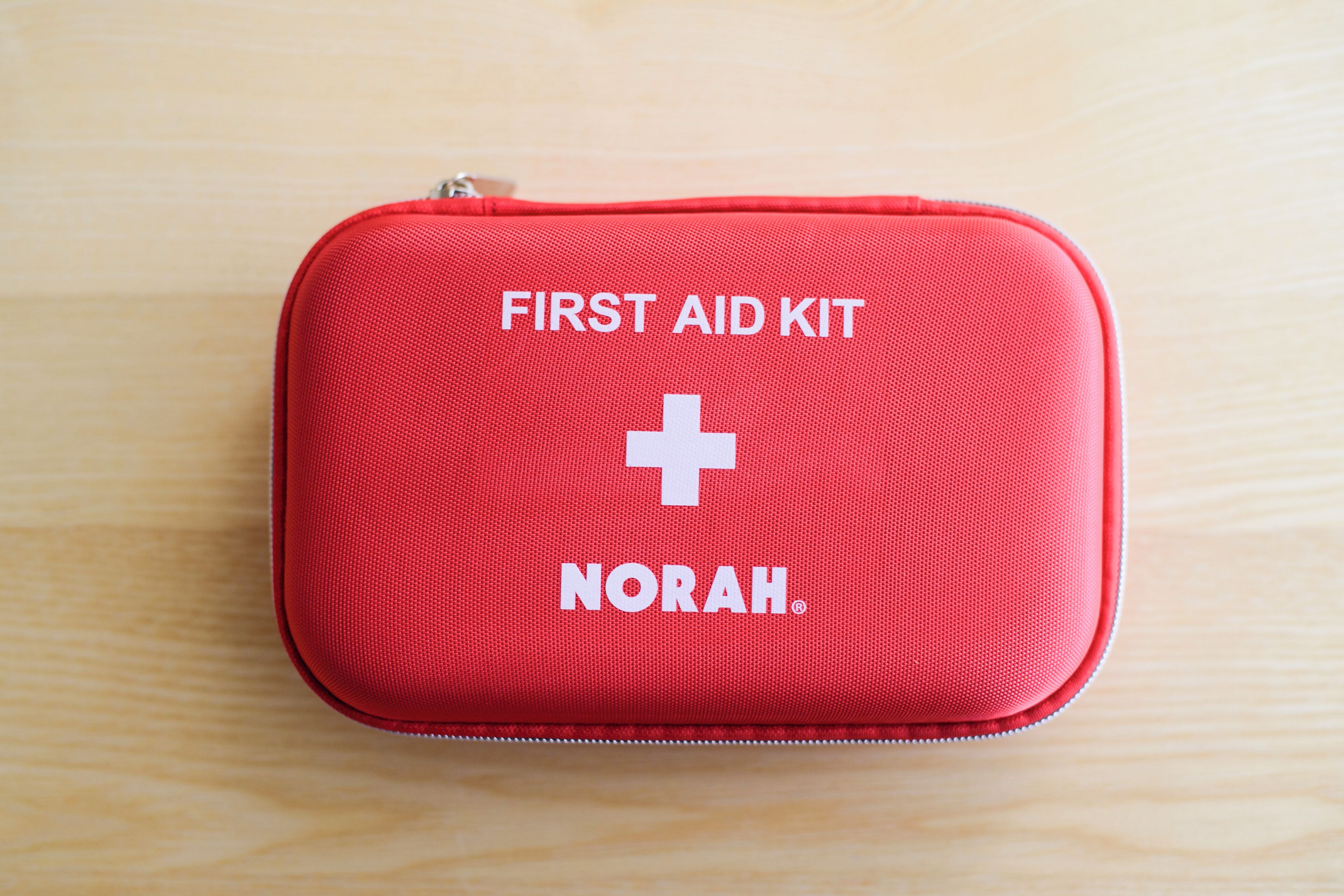 Um kit de primeiros socorros vermelho com os dizeres 'FIRST AID KIT' e 'NORAH'.