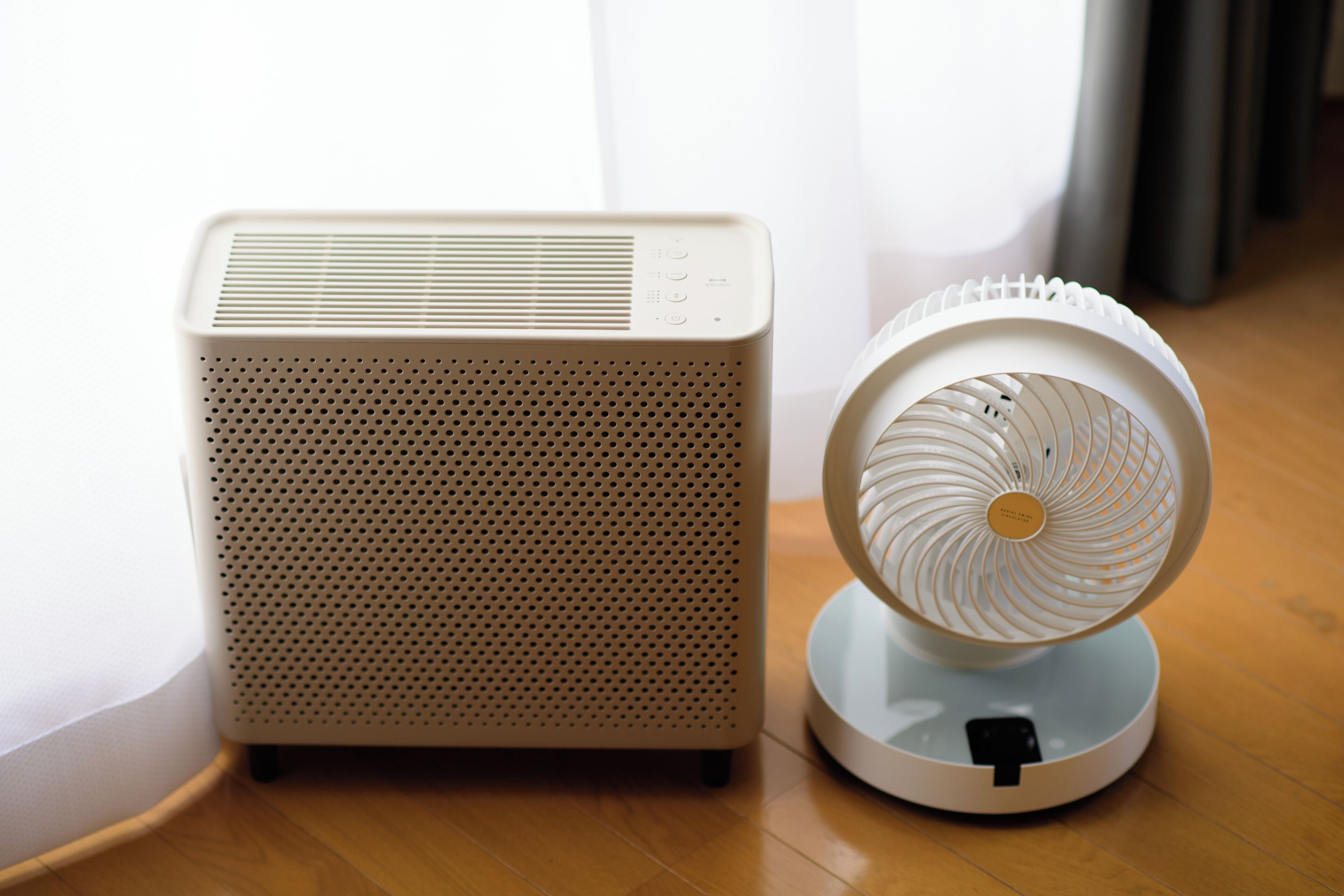 A portable air purifier and a standing fan on a wooden floor.