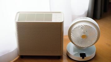 A portable air purifier and a standing fan on a wooden floor.