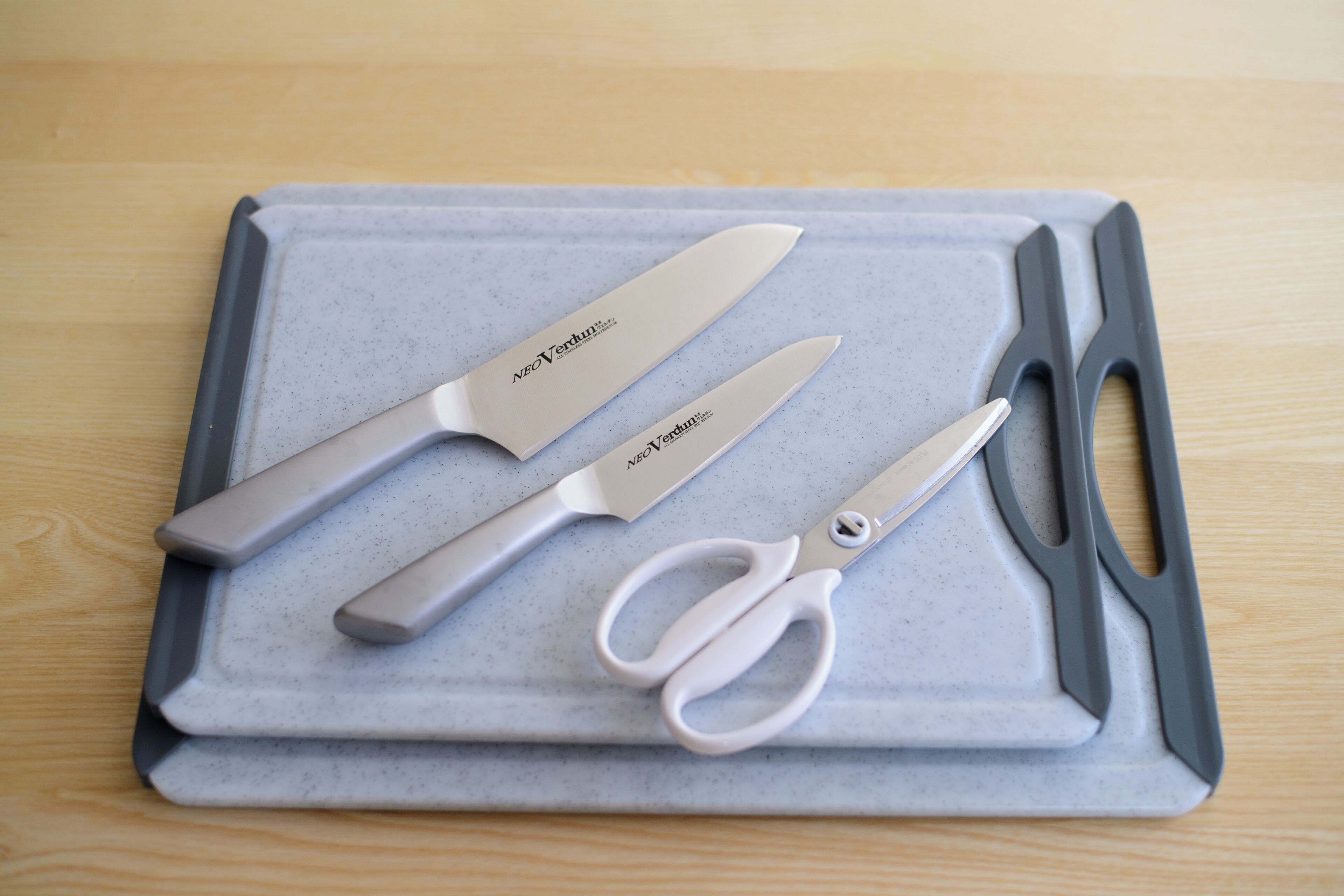 A set of three knives and a pair of scissors on a gray tray.