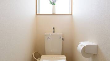 A compact bathroom with a toilet, a small window with a plant, and a wall-mounted toilet paper holder.