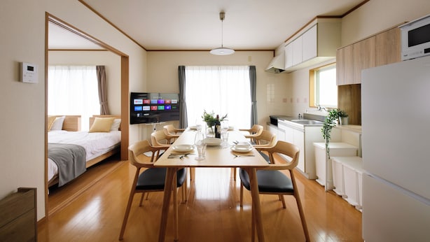 A modern, well-lit room with a dining table set for four, a bed with a TV, and a kitchen area. - Guest Villa Hakone Kazamatsuri (Odawara)