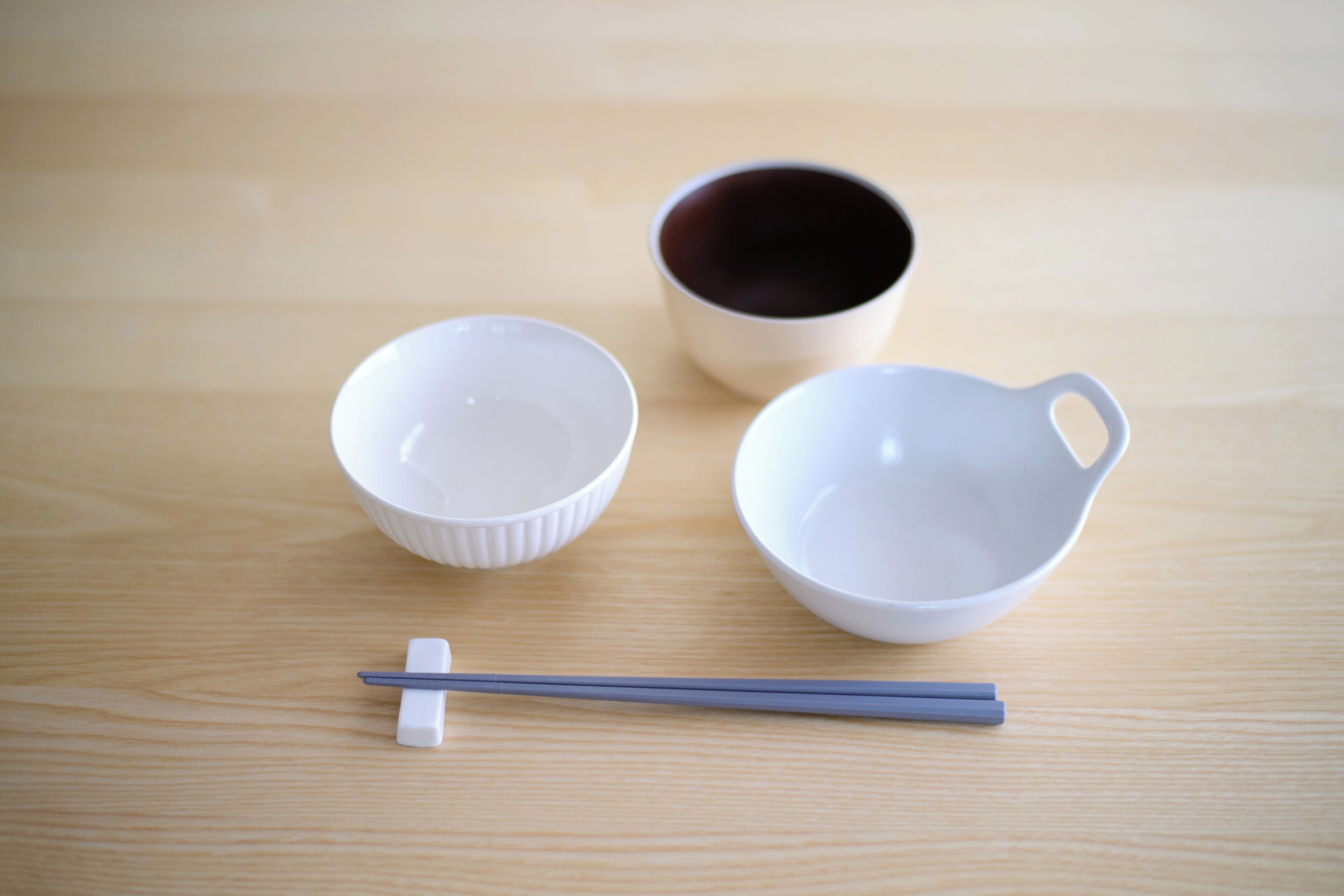 Three white bowls and a pair of chopsticks on a wooden surface.