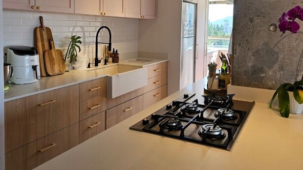 A modern kitchen with wooden cabinets, a white countertop, a gas stove, and a hanging plant. - Sunrise apartment (Itajaí)