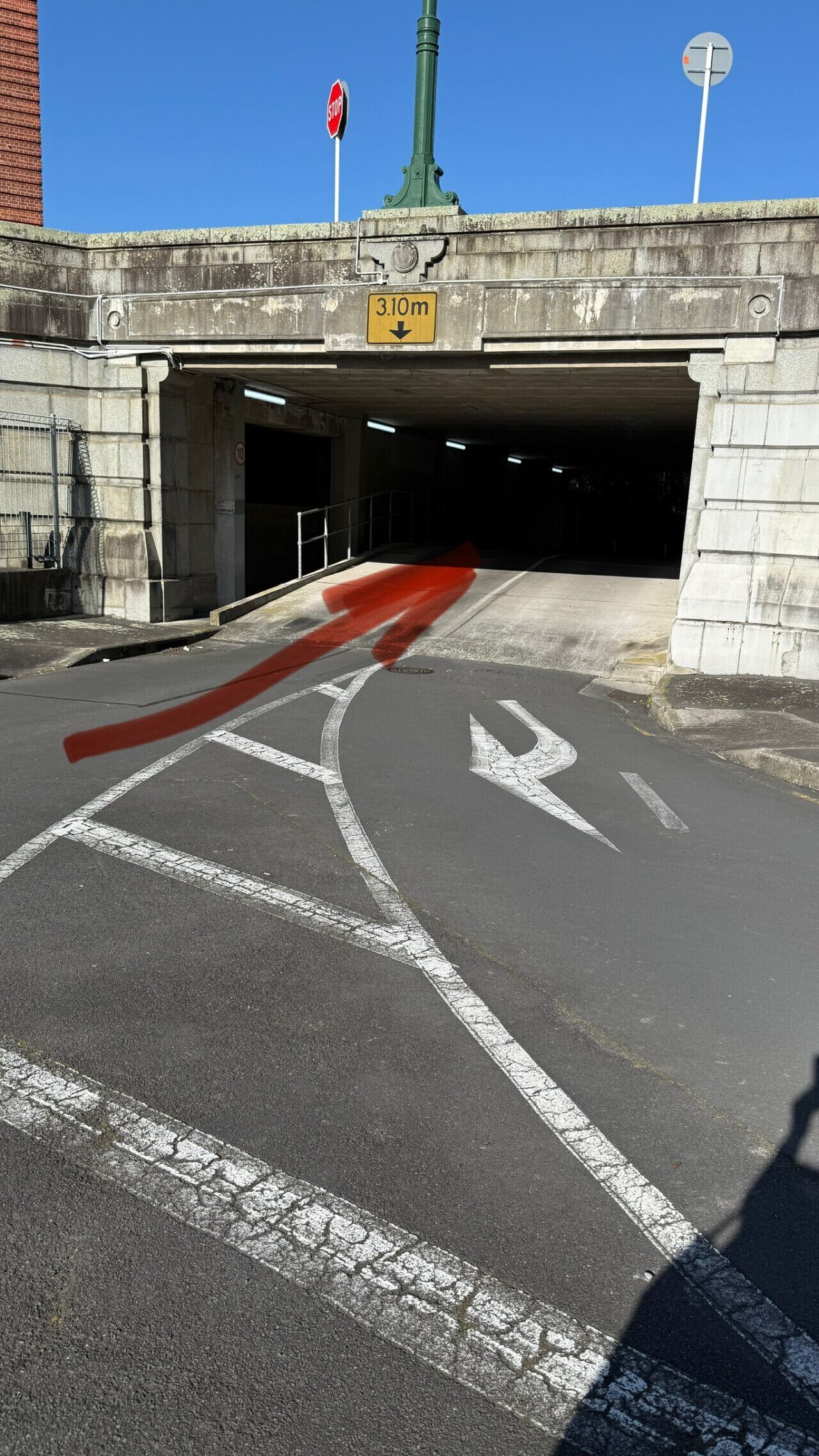 Ingresso di un parcheggio con un segnale di stop, un cartello con limite di altezza e frecce direzionali sull'asfalto.