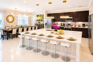 A modern kitchen with dark wood cabinets, stainless steel appliances, and a central island with bar stools. - 27-bedroom luxury villa near Disney (Kissimmee)