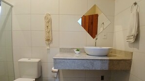 Un baño con inodoro, lavamanos con espejo, una planta pequeña y un cesto de basura.