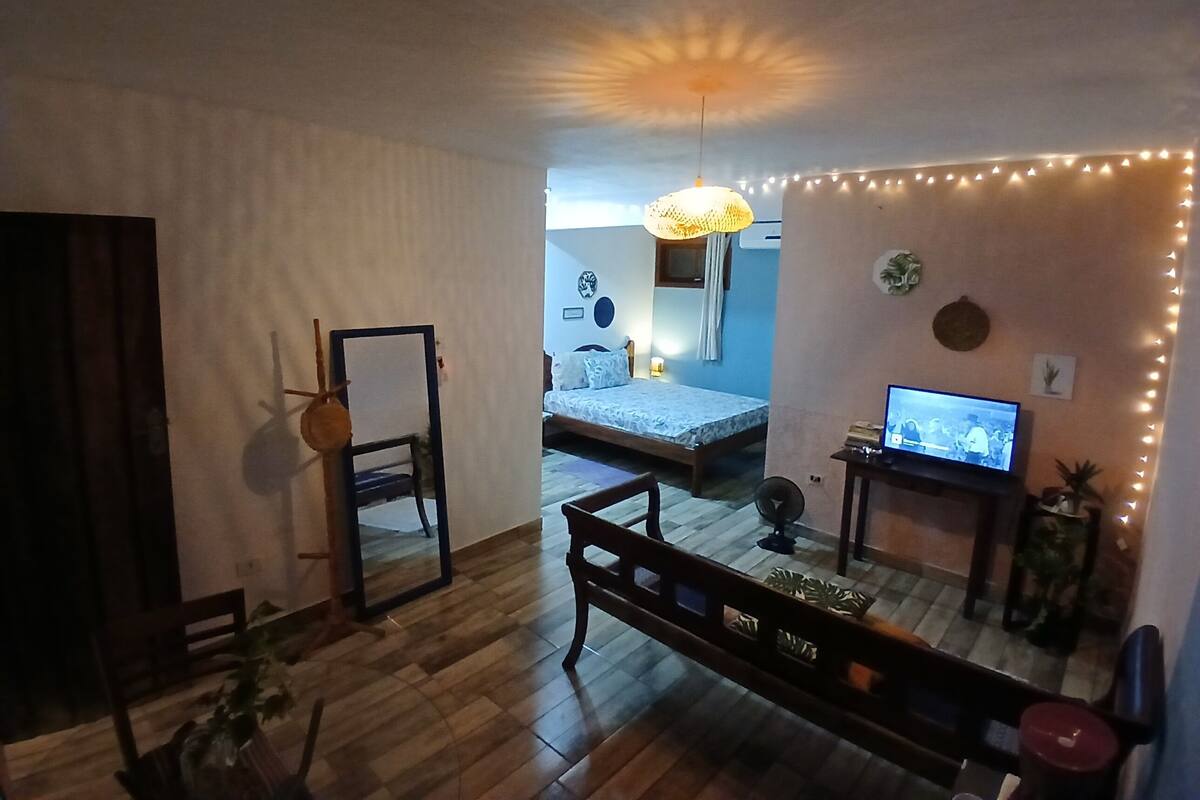 A room with a bed, a desk with a computer, a mirror, and a hanging light fixture.