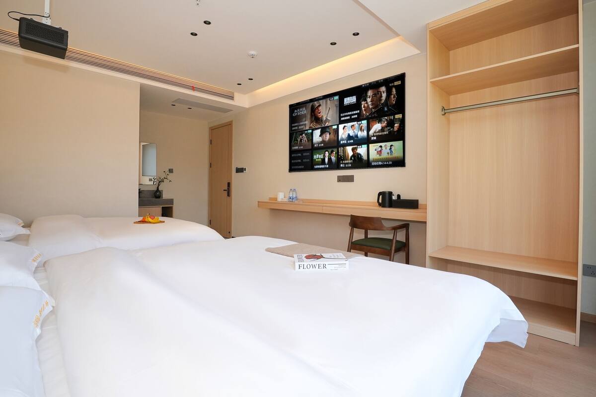 A hotel room with a large bed, a desk, a TV mounted on the wall, and a wardrobe.
