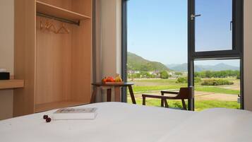 A hotel room with a large window, a bed, a small table with fruit, and a wooden wardrobe.