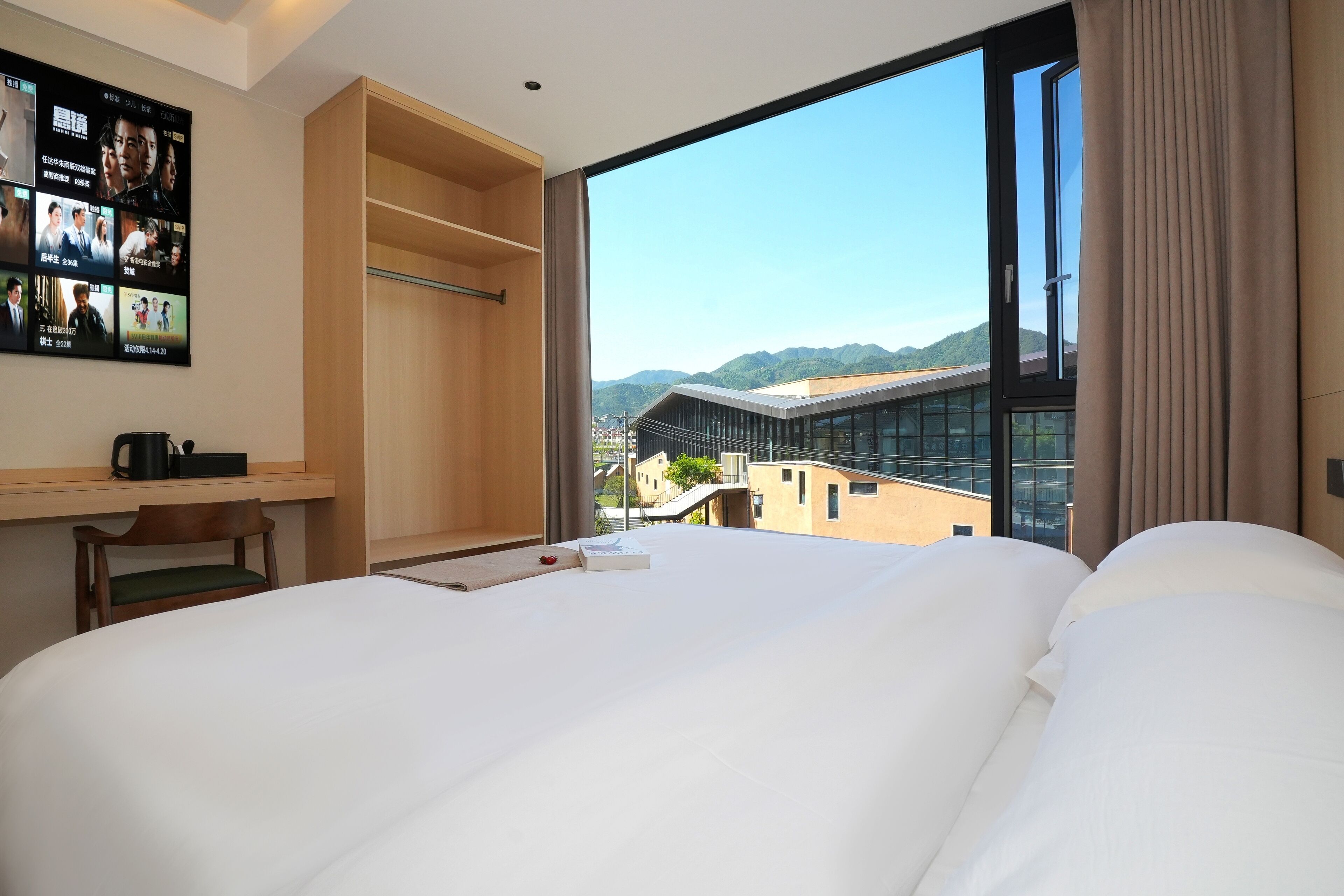 A hotel room with a large bed, a wooden desk, a chair, and a TV displaying movie posters.