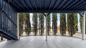 An outdoor covered area with a concrete floor, metal railing, and a view of tall trees and a road in the background. - Premium Cozy 1-bedroom apartment in fantastic Sacramento w/ AC and gym equipment (Sacramento)