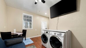 A laundry room with two front-loading washers and dryers, a dining table with chairs, a blue couch, and a TV mounted on the wall. - Premium Cozy 1-bedroom apartment in fantastic Sacramento w/ AC and gym equipment (Sacramento)