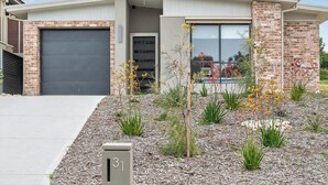 Ein modernes Haus mit Backsteinfassade, Garage und einem gepflegten Garten mit verschiedenen Pflanzen und Blumen.