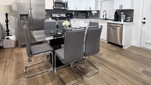 A modern kitchen with white cabinets, stainless steel appliances, and a dining area with grey chairs.