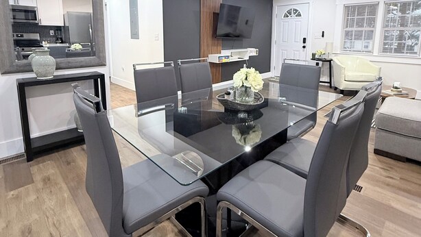 A modern dining area with a glass-top table, grey upholstered chairs, and a central vase with flowers.