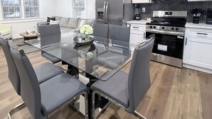 A modern kitchen with white cabinets, stainless steel appliances, and a glass dining table with chairs.