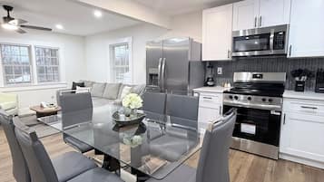 A modern kitchen with white cabinets, stainless steel appliances, and a glass dining table with chairs.