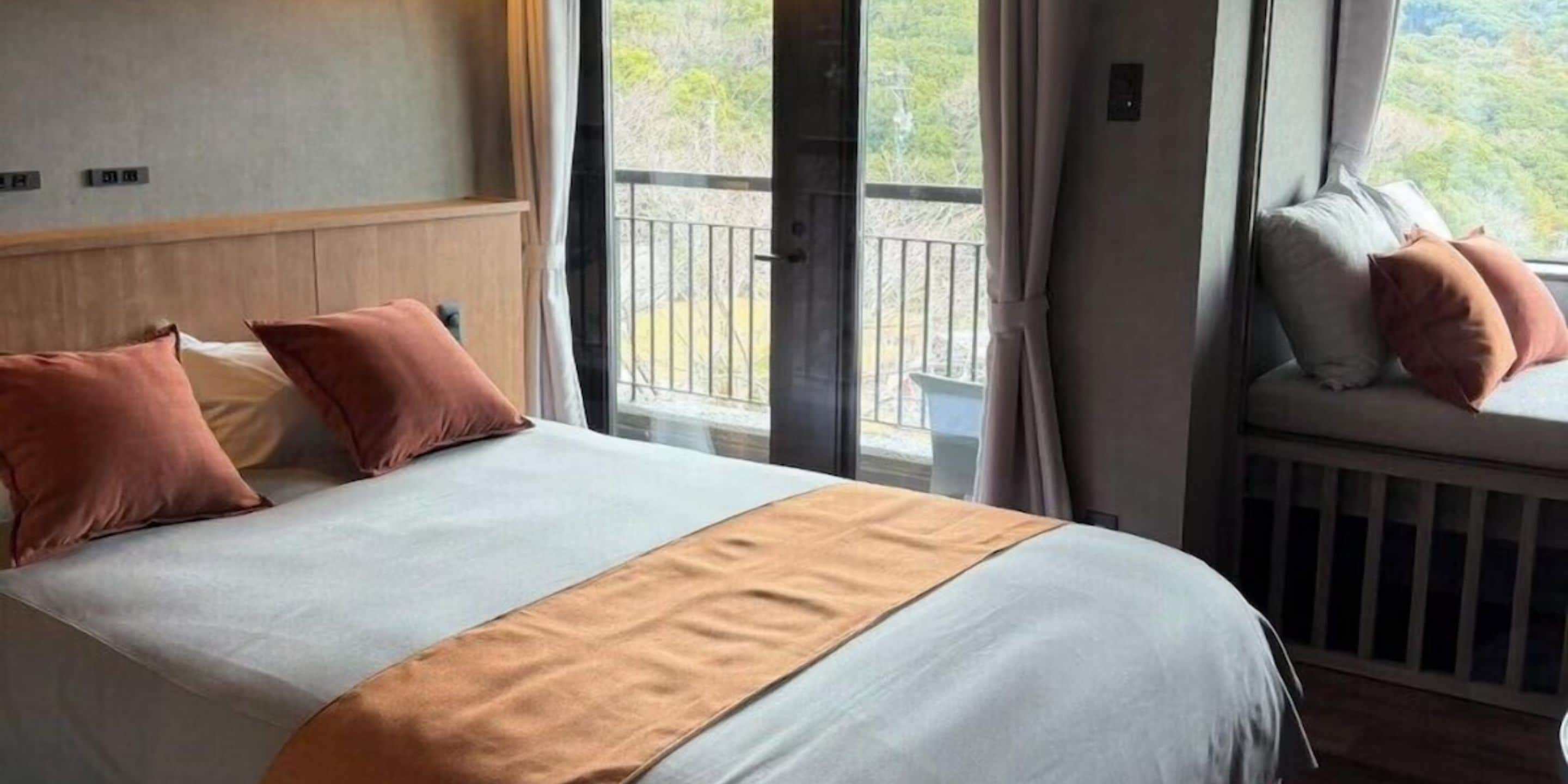 Habitación de hotel con una cama grande, vistas al exterior desde un balcón y una ventana con cortinas.