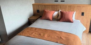 Habitación de hotel con cama, cabecera de madera, mesita de noche y dos interruptores en la pared.
