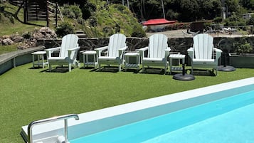 Zona junto a la piscina con sillas Adirondack blancas y una piscina azul.