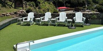 Zona junto a la piscina con sillas Adirondack blancas y una piscina azul.