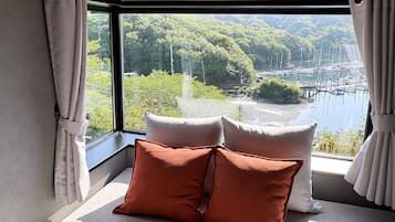 A room with a large window offering a view of a lake and docked boats. There are two pillows on a bench.