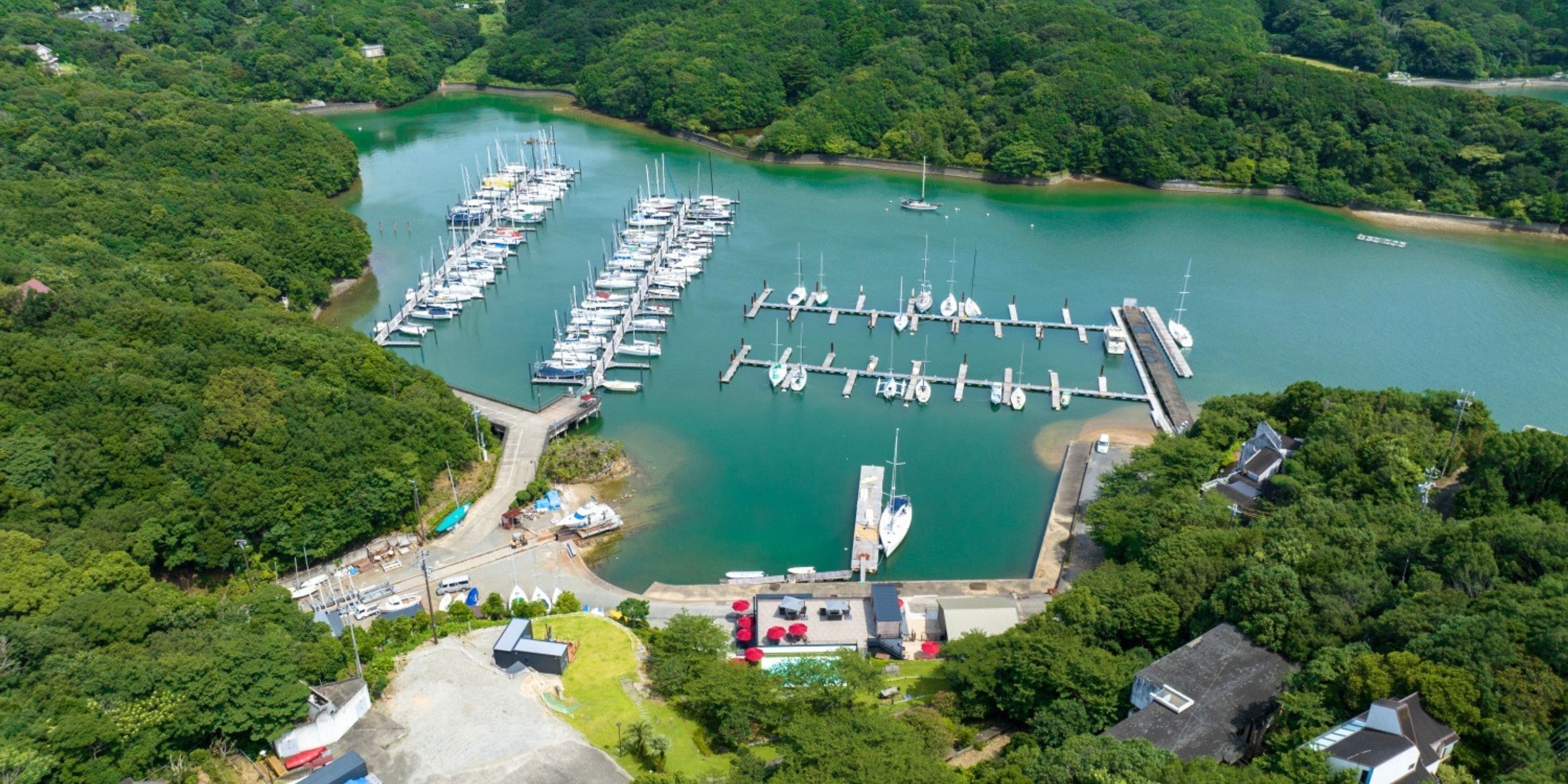 An aerial view of a marina with multiple docks and boats, surrounded by dense greenery.