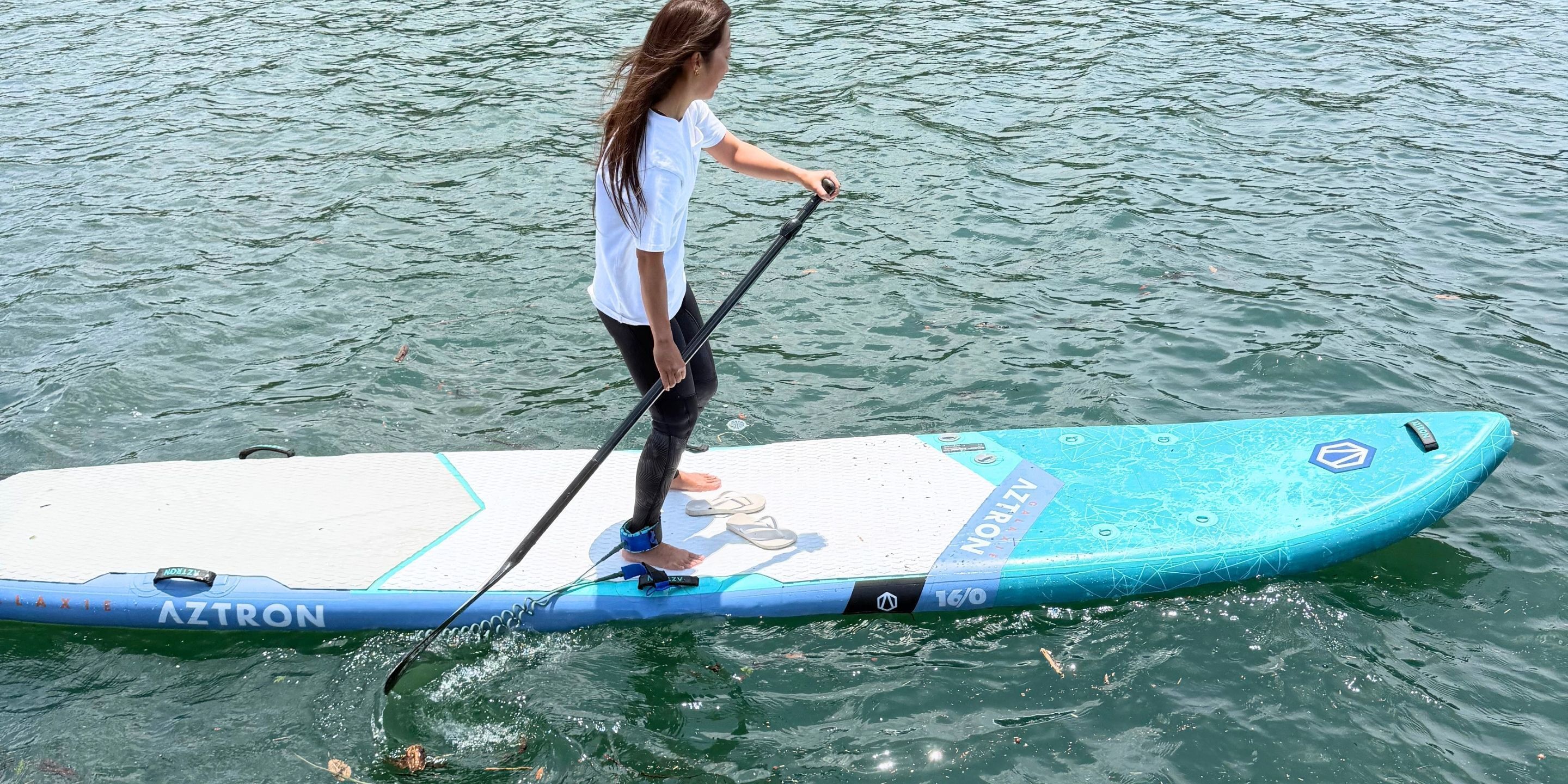 Une personne debout sur une planche de paddle, sur un plan d’eau.