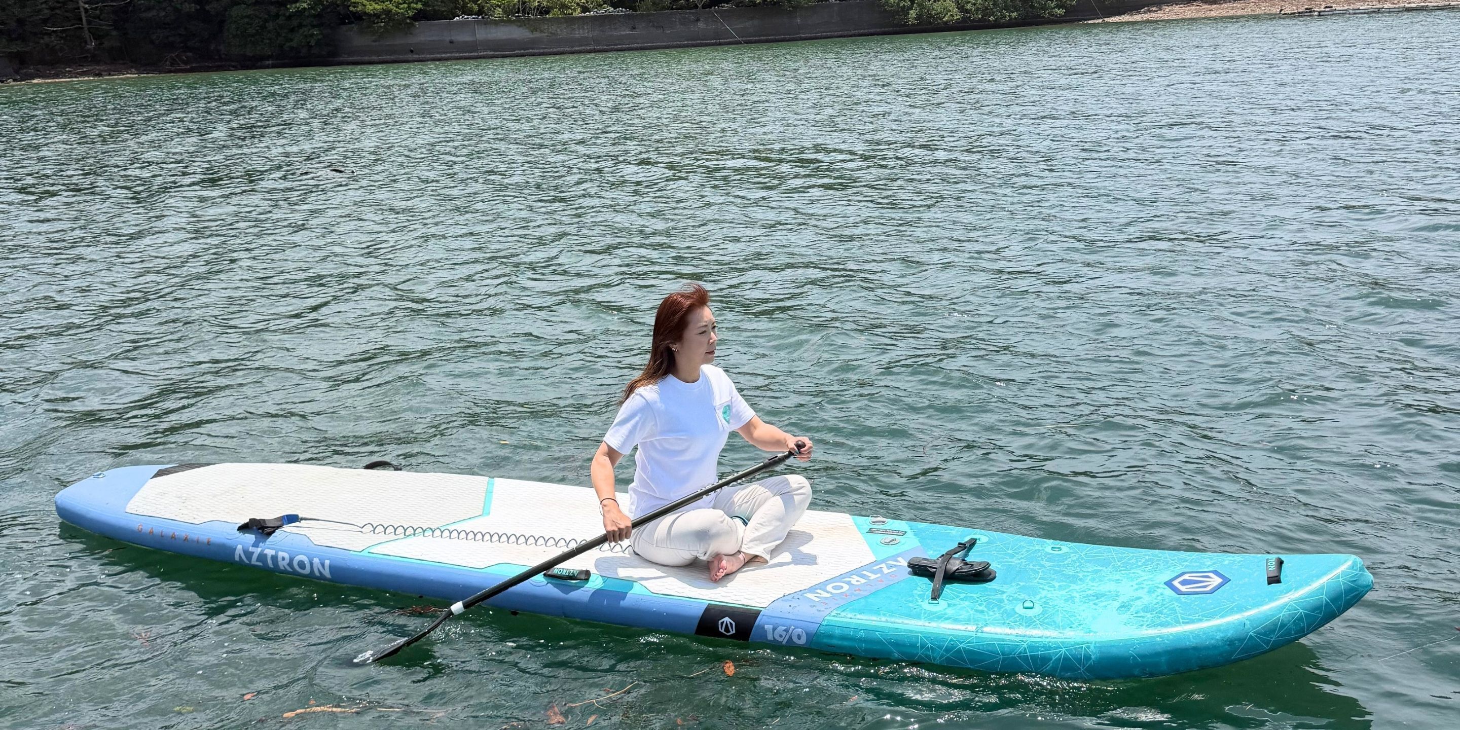 Una persona sentada en una tabla de remo azul y blanca sobre agua.