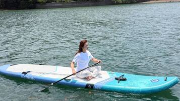 Una persona sentada en una tabla de remo azul y blanca sobre agua.