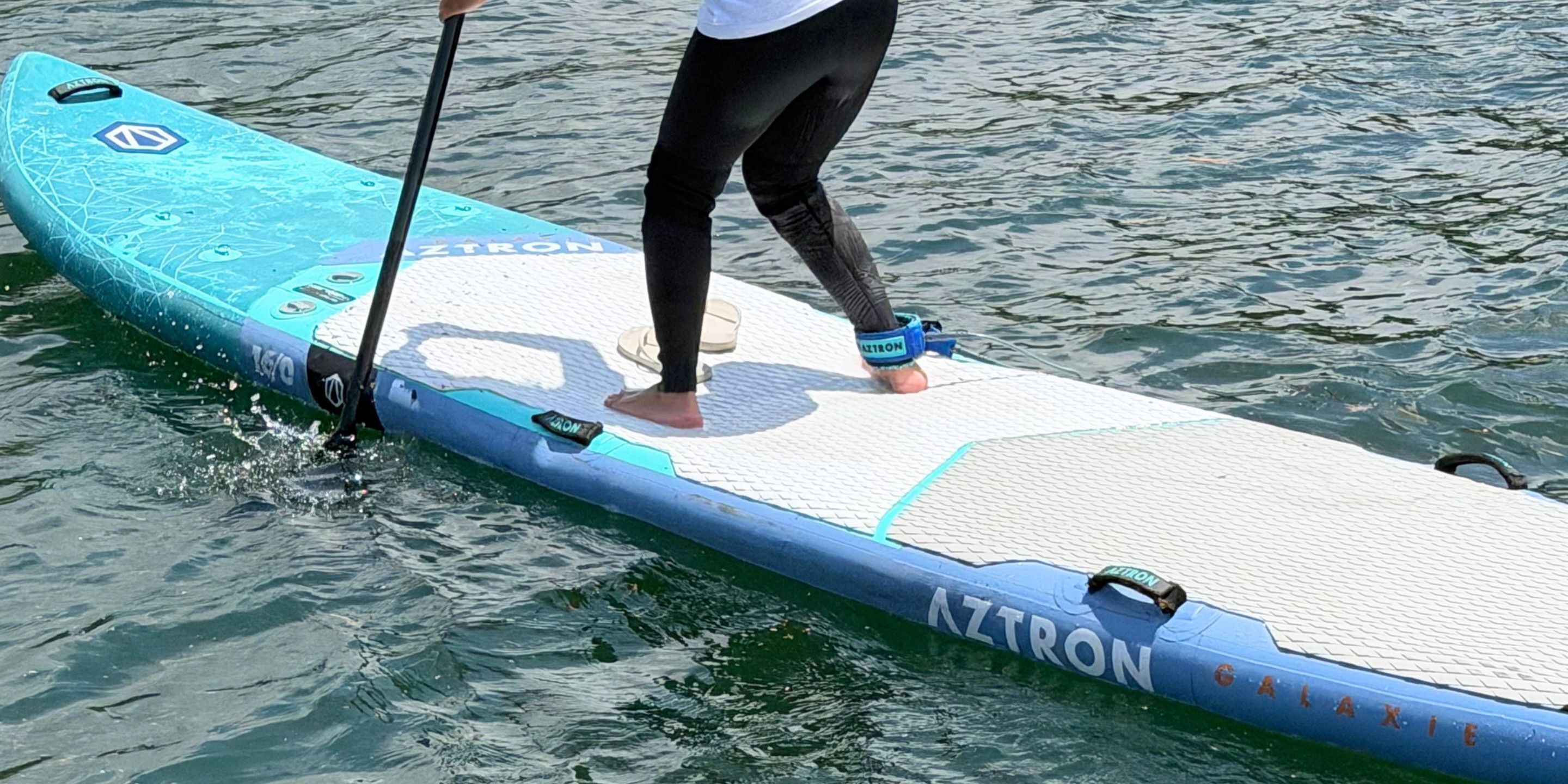 A person standing on a paddleboard with the brand name 'AZTRON' visible.