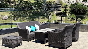 Un patio al aire libre con mobiliario de mimbre, incluyendo un sofá, dos sillones y una mesita.