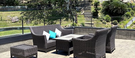 An outdoor patio with wicker furniture, including a sofa, two armchairs, and a small table.
