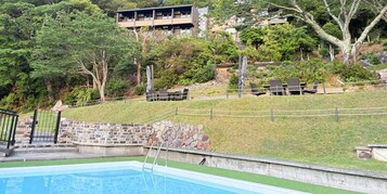 Una piscina con un muro de piedra y una zona ajardinada.