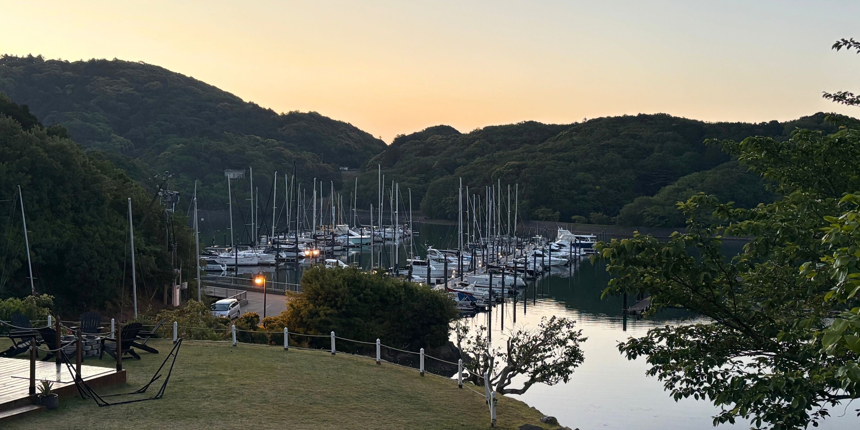 A marina with boats docked, surrounded by hills and greenery.