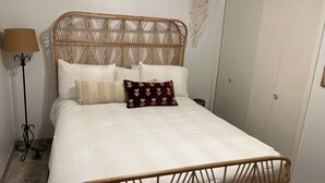 Ein Bett mit einem gewobenen Kopfteil, weißer Bettwäsche und einer Wanddekoration aus Makramee.