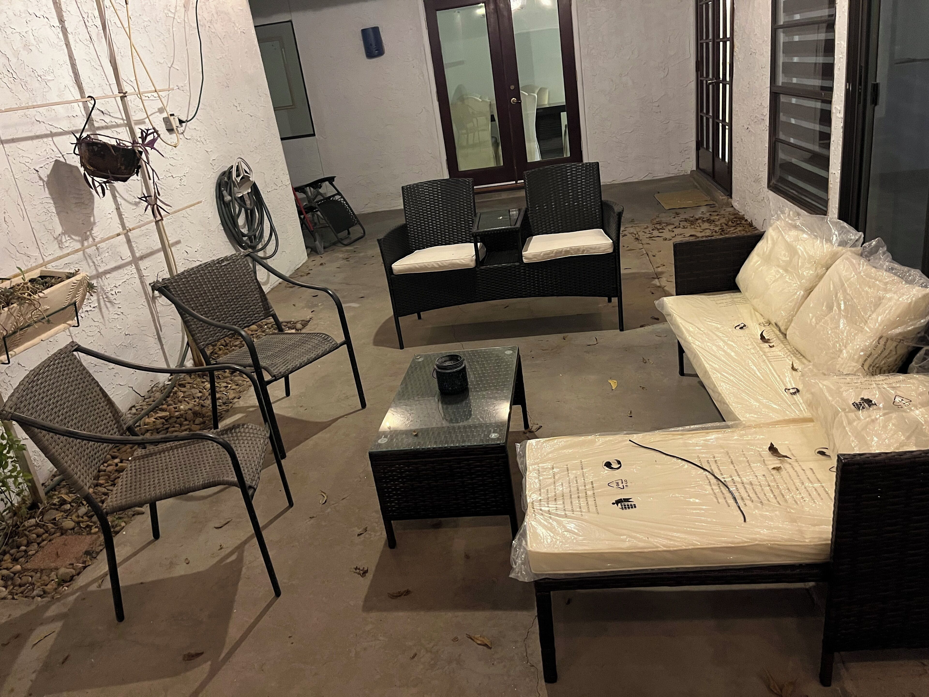Un espacio al aire libre con mobiliario de mimbre, una mesa pequeña y un sofá cubierto.