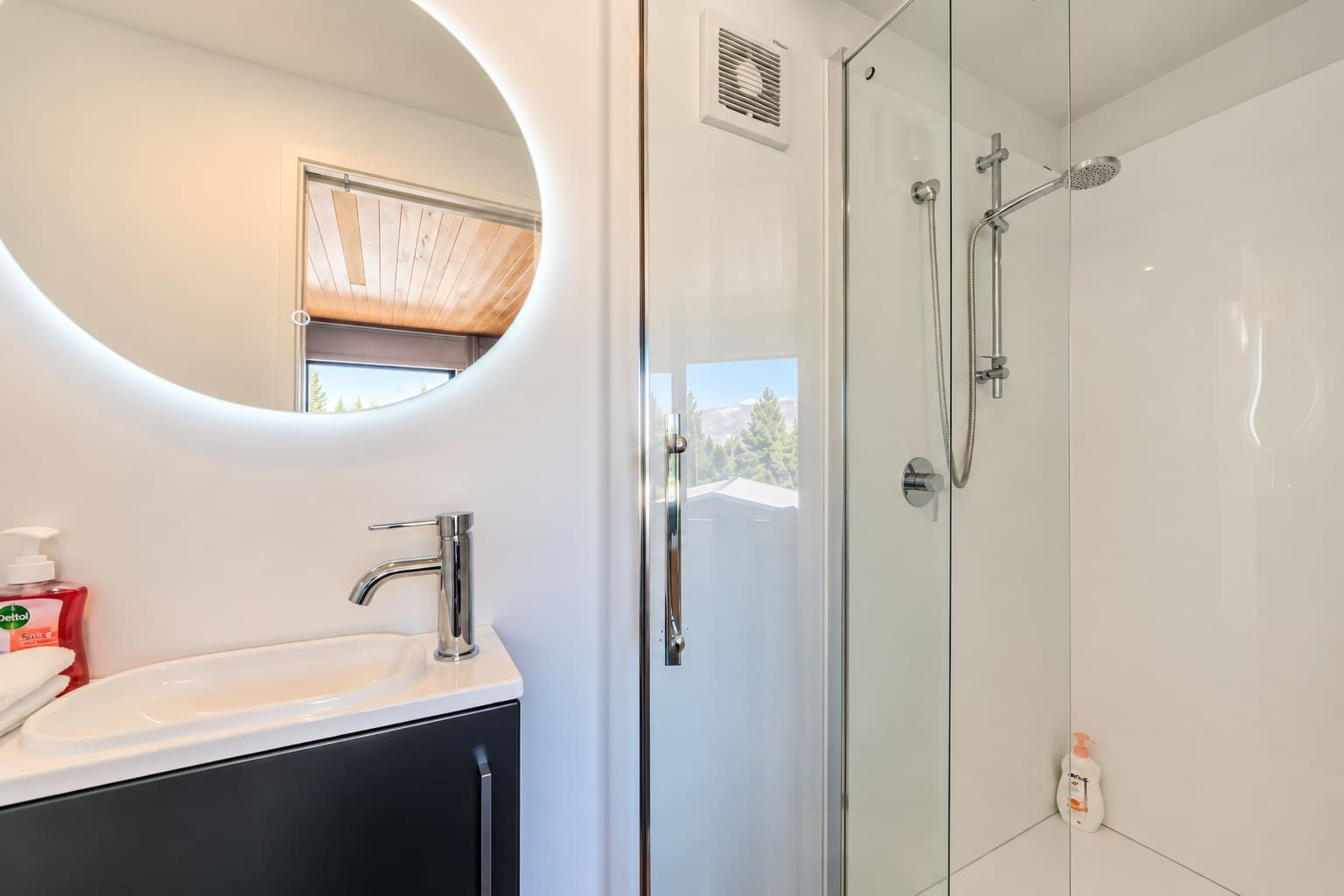 Un baño moderno con ducha de vidrio, un espejo redondo y un lavamanos blanco.