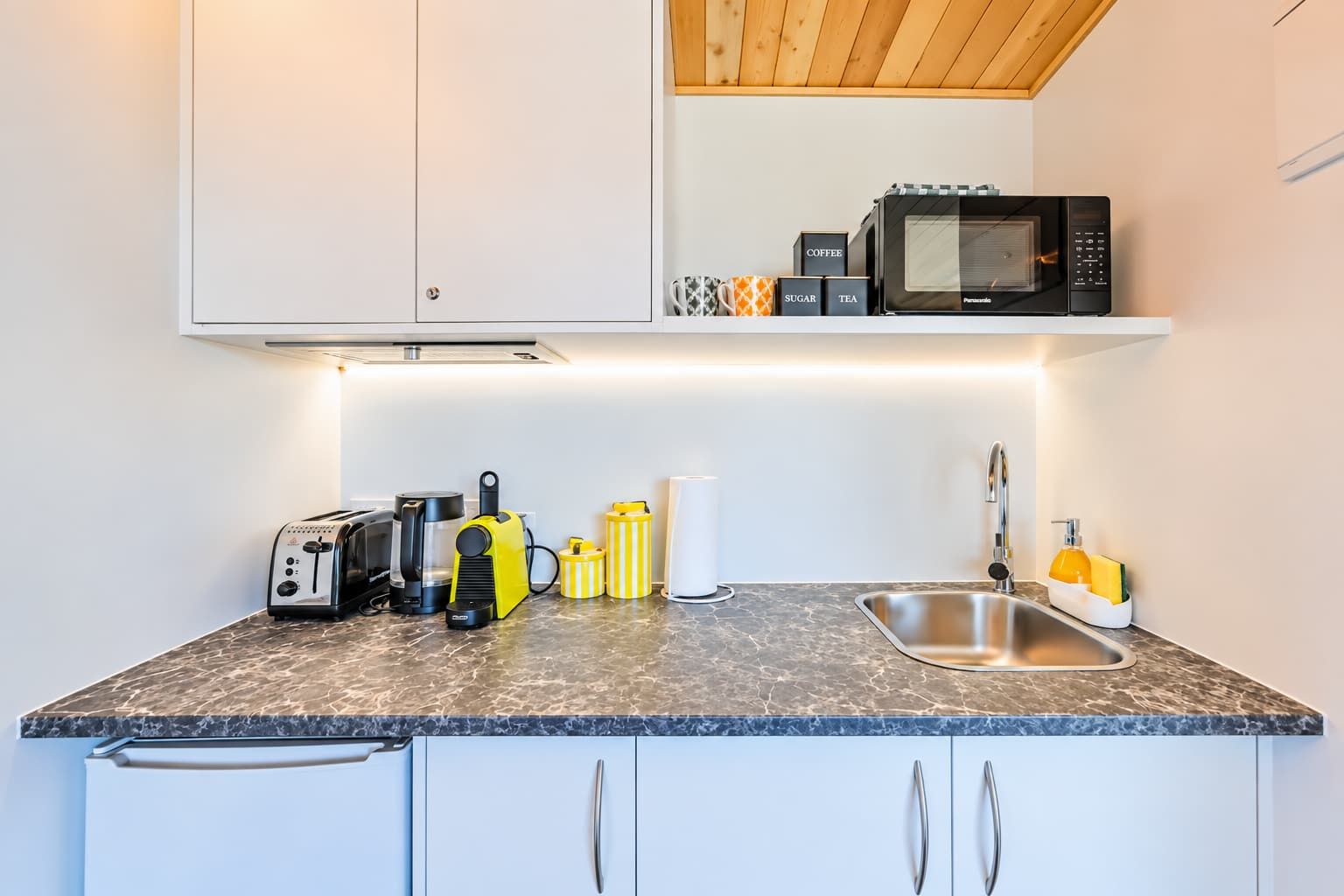Een kleine keuken met een magnetron, broodrooster, koffiezetapparaat en een spoelbak.