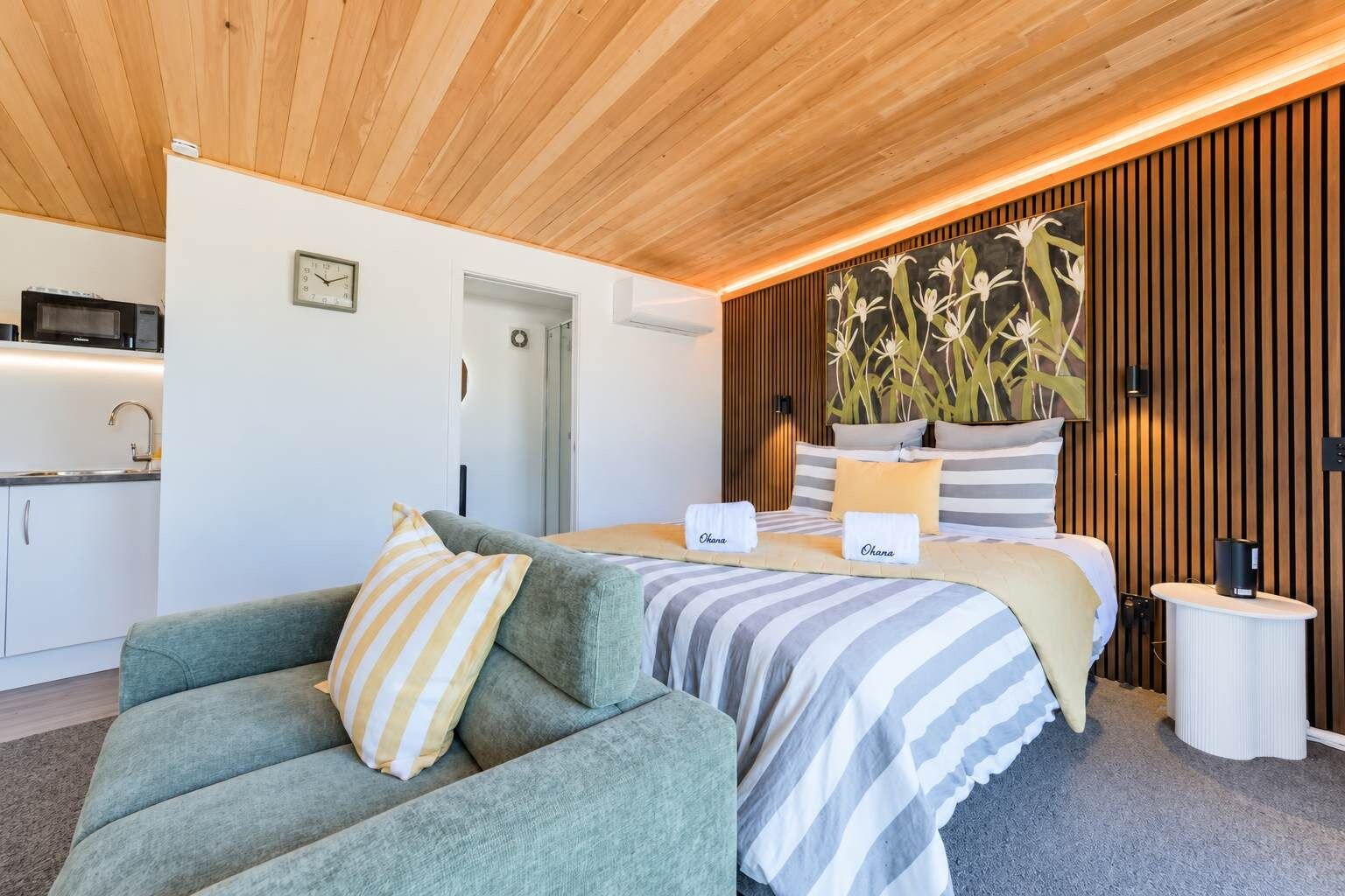 Ein modernes Schlafzimmer mit einem Bett, einem grünen Sofa, einer Küchenzeile und einer Holzbalkendecke.
