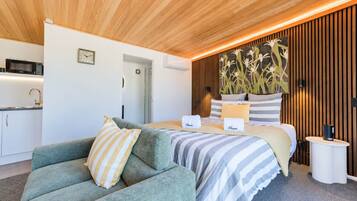 Ein modernes Schlafzimmer mit einem Bett, einem grünen Sofa, einer Küchenzeile und einer Holzbalkendecke.