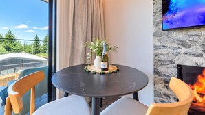 Et rundt bord med en flaske vin og en vase blomster, en pejs og et fjernsyn monteret på en stenvæg.