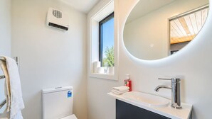 Et moderne badeværelse med toilet, håndvask, spejl og et vindue.