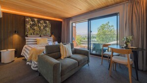 Ein modernes Hotelzimmer mit Bett, Sofa, Esstisch und einem Balkon mit Blick.