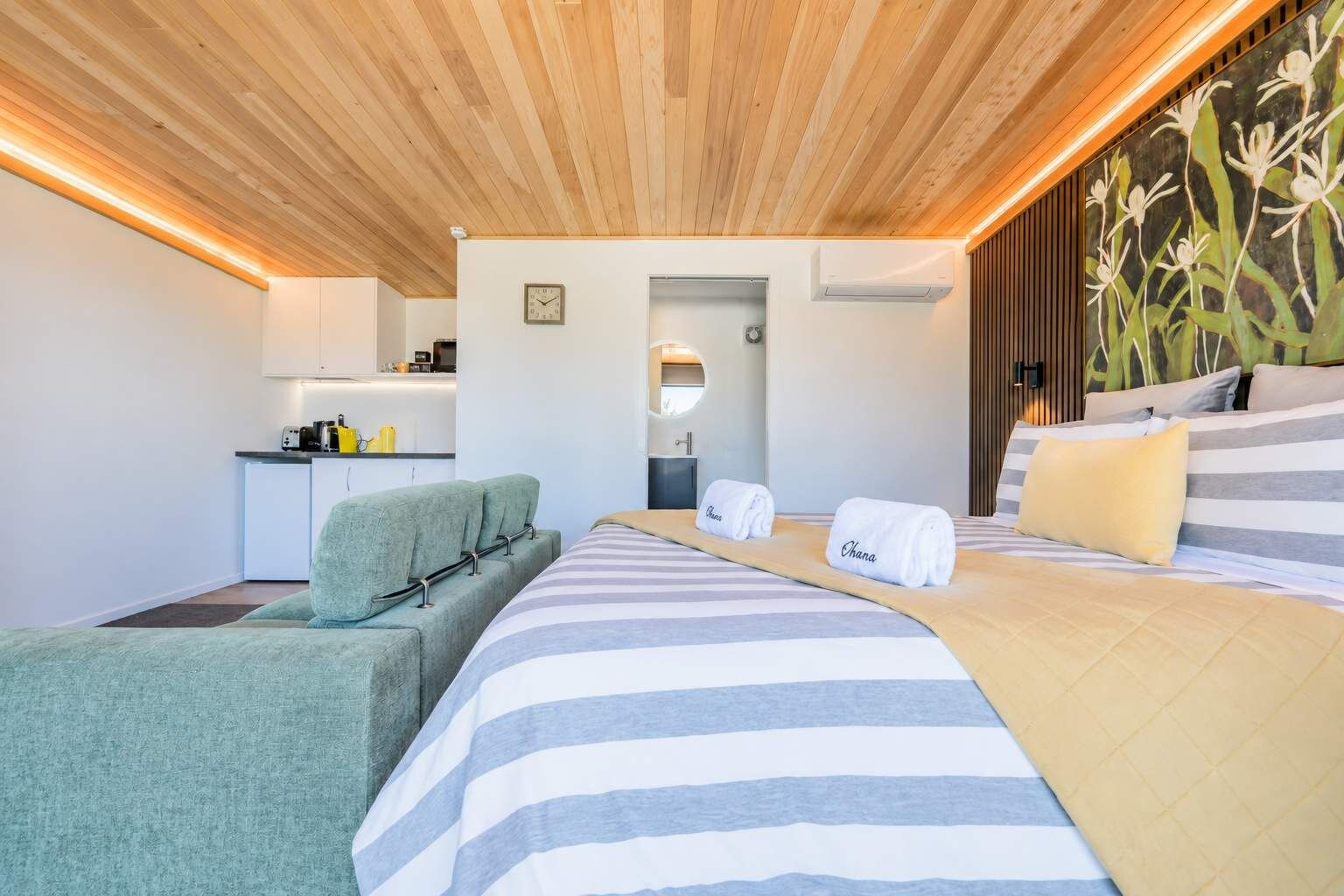 A hotel room with a bed, a sofa, a small kitchenette, and a bathroom.