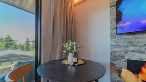 Ein runder Tisch mit einer Weinflasche und einem Blumenstrauß, hölzerne Stühle, eine Steinwand und ein an der Wand befestigter Fernseher.