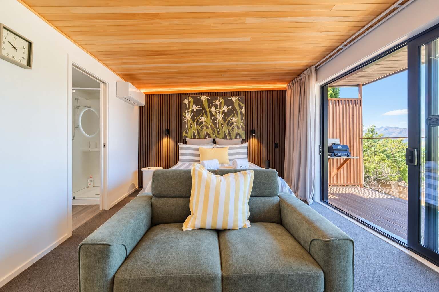 A modern bedroom with a bed, a sofa, and a large window offering a view of the outdoors.