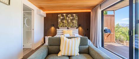 A modern bedroom with a bed, a sofa, and a large window offering a view of the outdoors.