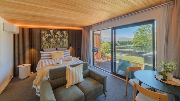 Ein modernes Schlafzimmer mit einem großen Bett, einer Couch, einem Esstisch und einer Glasschiebetür zu einem Außenbereich.